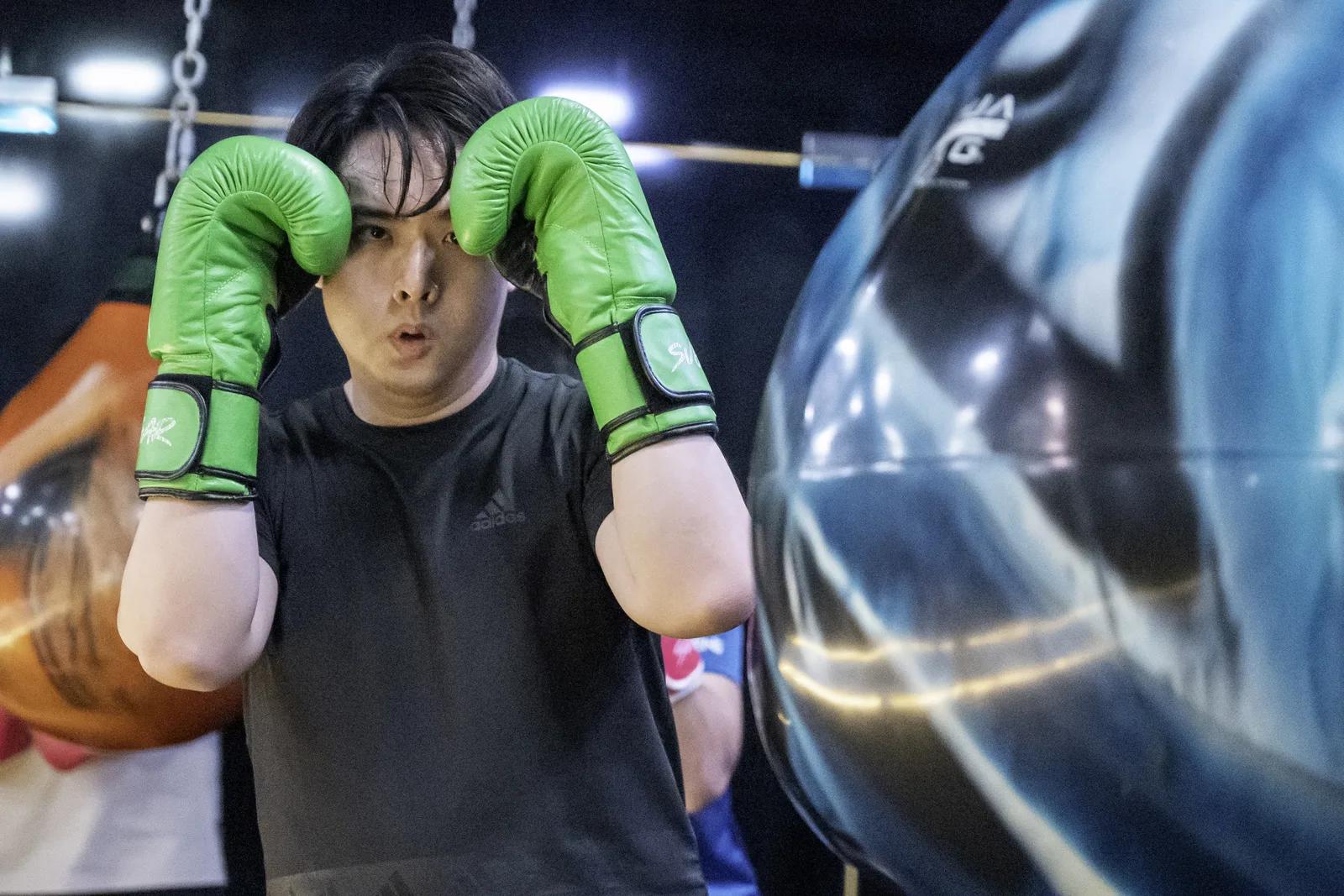 Boxer training behind a motion-blurred punching bag in low-key light