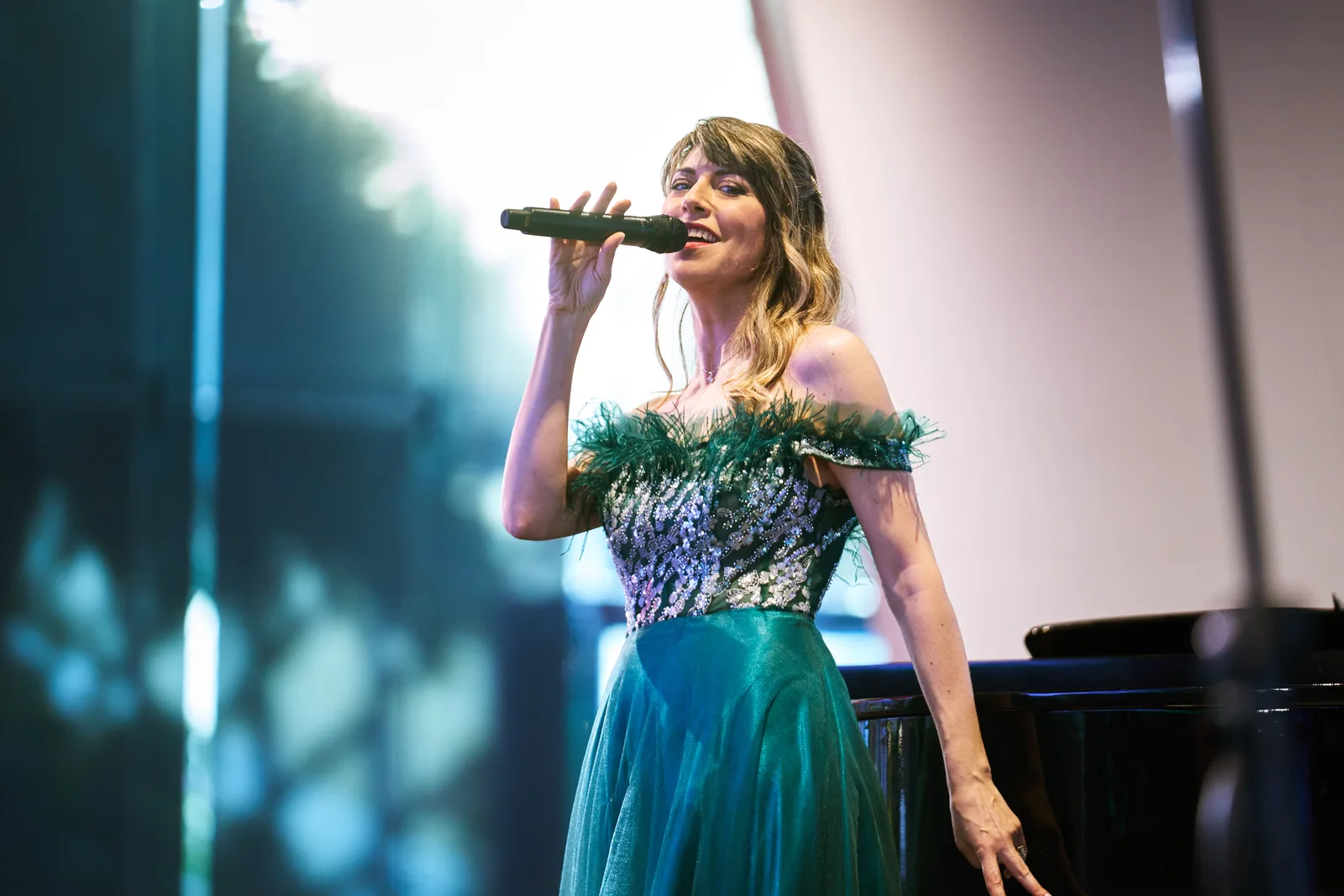 Singer in a green sequined gown performing at a grand piano under stage lighting at a gala dinner