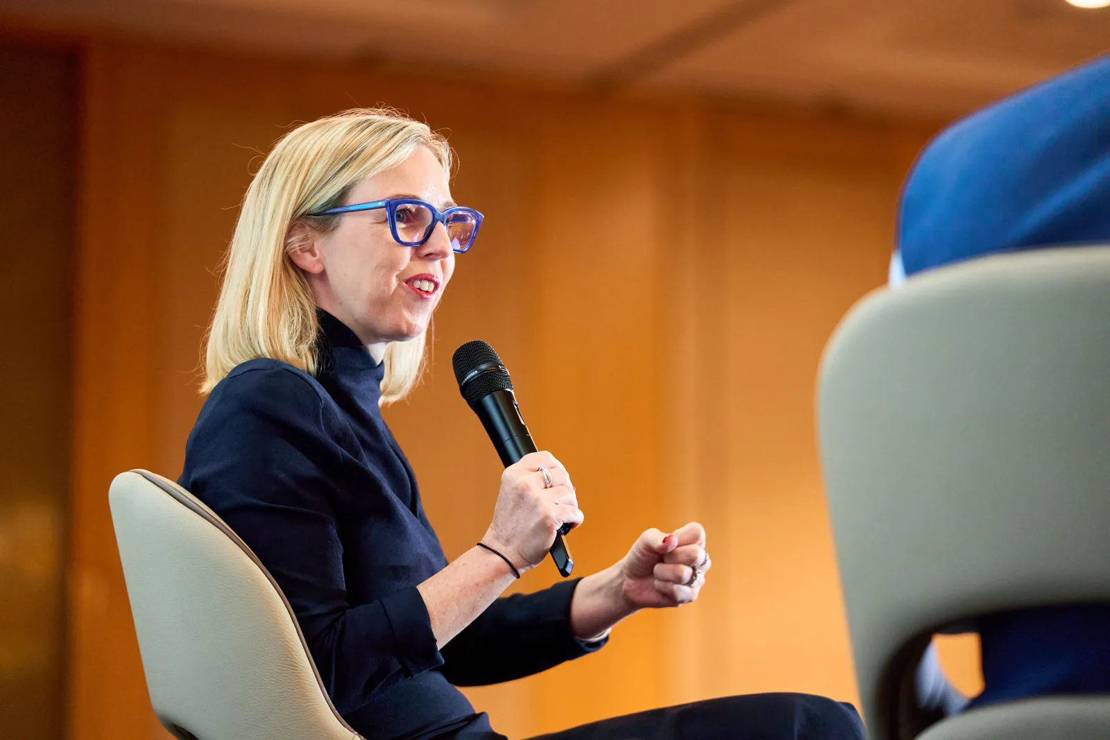 Seated conference panellist speaking into a microphone with expressive hand gestures