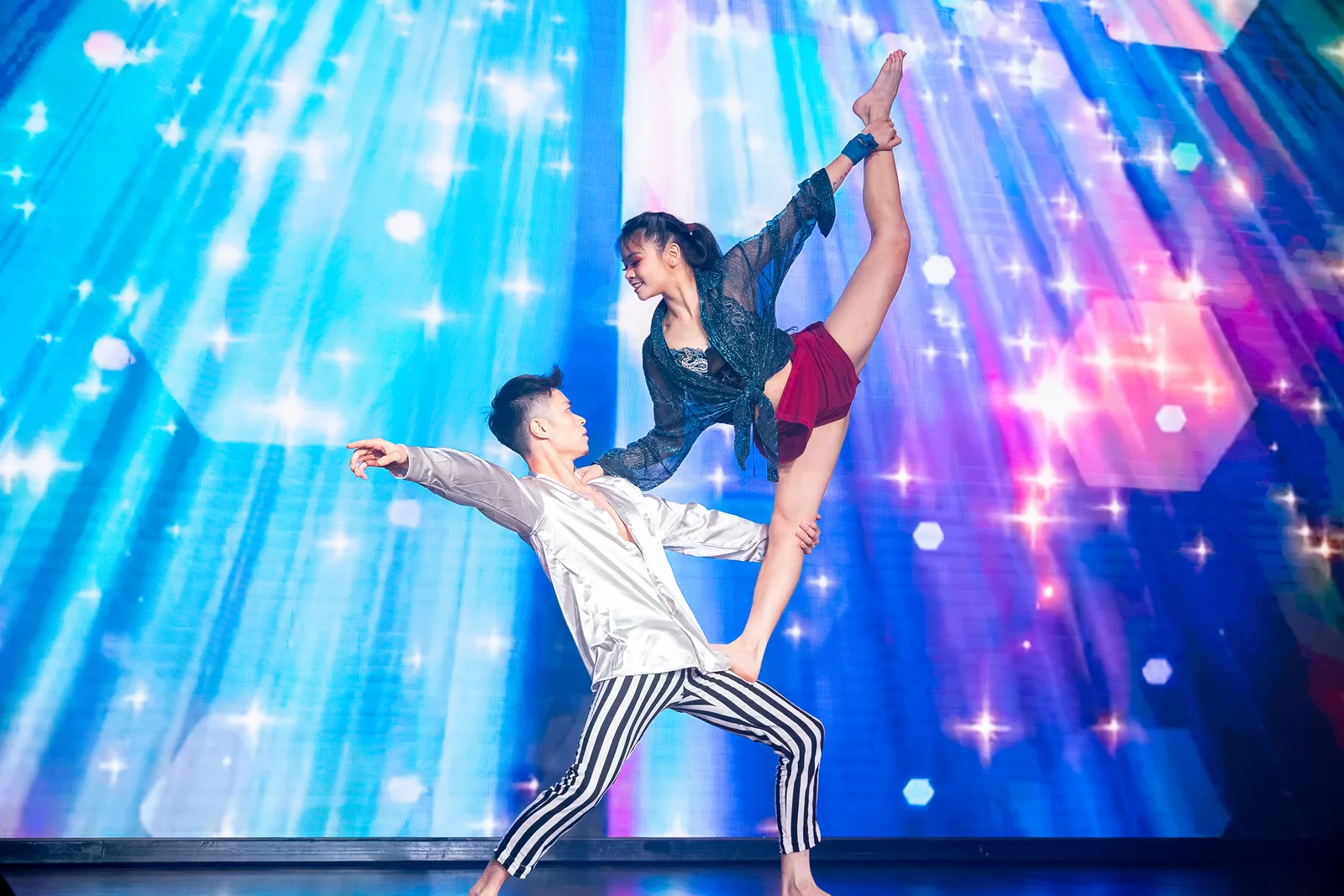 Aerial acrobatic duo mid-pose against a blue and purple LED stage backdrop at a corporate event