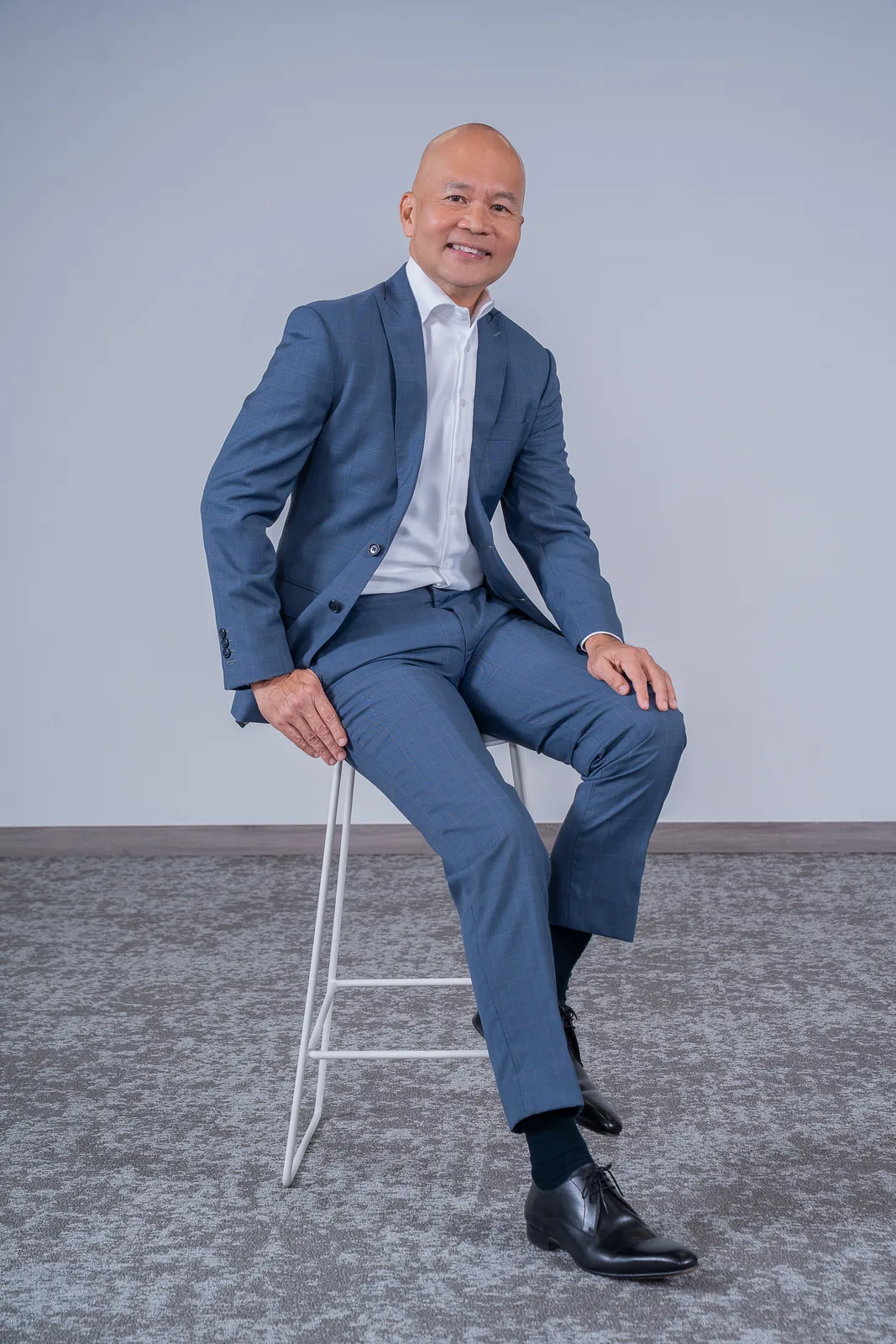 Full-length corporate portrait of an executive seated against a neutral studio backdrop