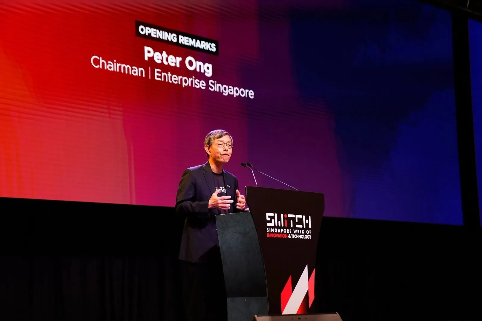 Keynote speaker delivering opening remarks at a podium under stage lighting — RS Photography